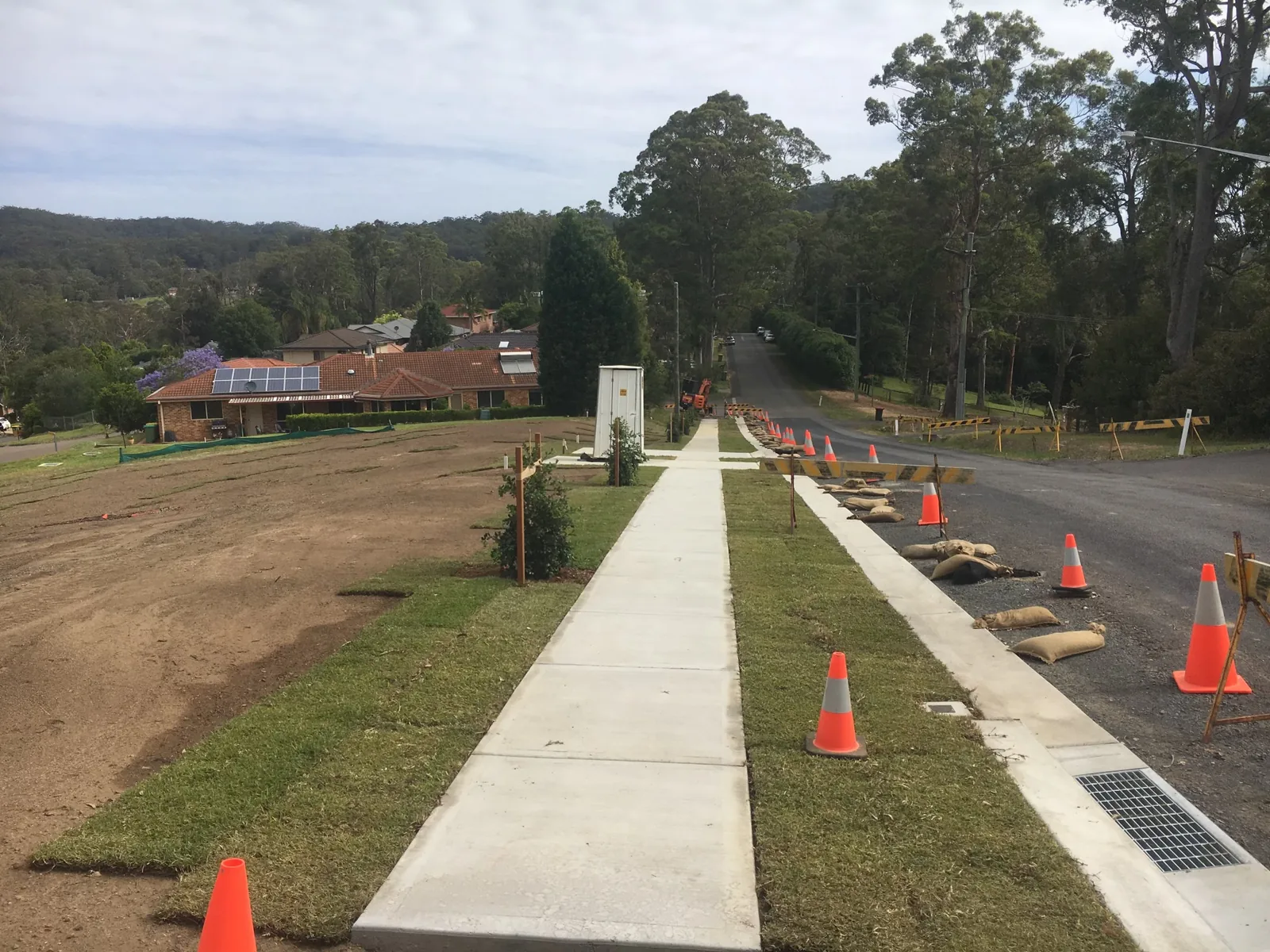 New concrete pathway and grated drainage installed beside a road