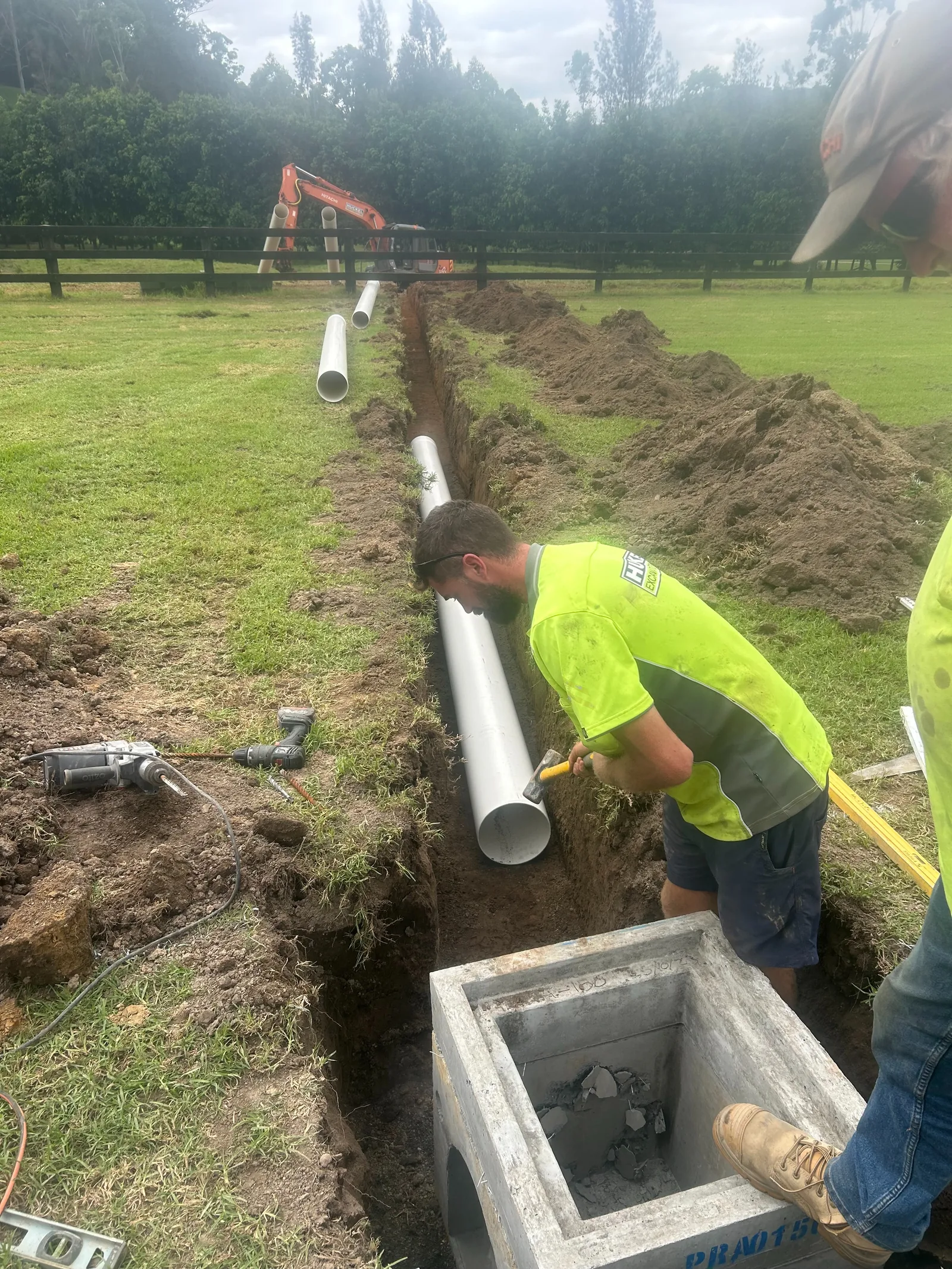 Drainage pipe being installed in a narrow excavated trench across a grassed property