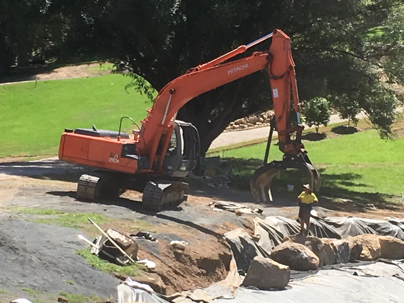 Huckel excavator positioning sandstone around a lined landscape area